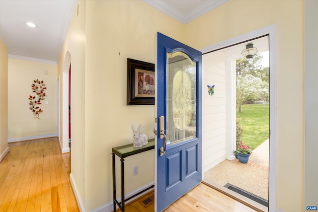 entryway featuring crown molding, arched walkways, baseboards, and light wood-style flooring