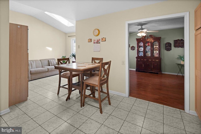 dining space featuring a skylight, baseboards, ceiling fan, and light tile patterned flooring