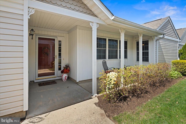 doorway to property with a porch and a shingled roof