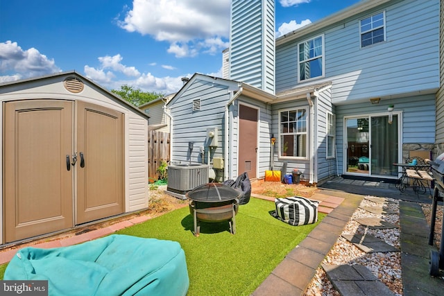 rear view of property with an outdoor fire pit, a storage shed, central AC unit, a chimney, and an outbuilding