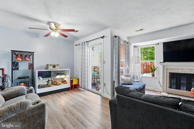 living area featuring a ceiling fan, a textured ceiling, visible vents, wood finished floors, and a premium fireplace