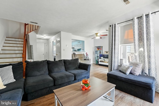 living room with visible vents, a ceiling fan, wood finished floors, and stairway