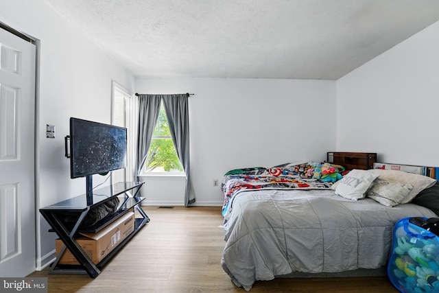 bedroom with baseboards, a textured ceiling, and wood finished floors