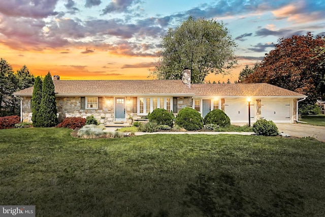 view of front facade featuring a front lawn, stone siding, a chimney, an attached garage, and driveway