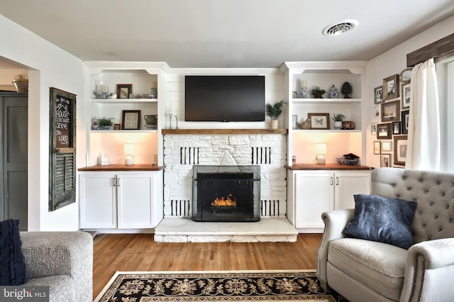 living room with visible vents, built in shelves, wood finished floors, and a stone fireplace