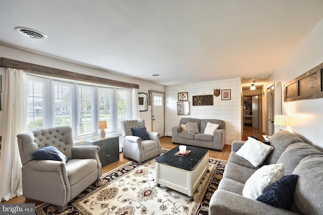 living room with wood walls, visible vents, and light wood-style floors