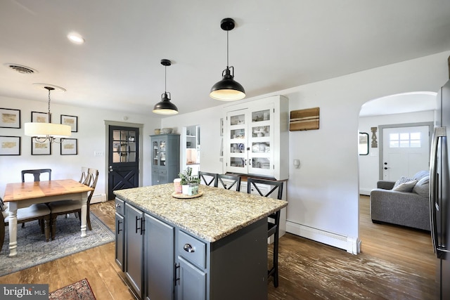 kitchen featuring visible vents, arched walkways, a kitchen breakfast bar, a baseboard heating unit, and dark wood-style floors