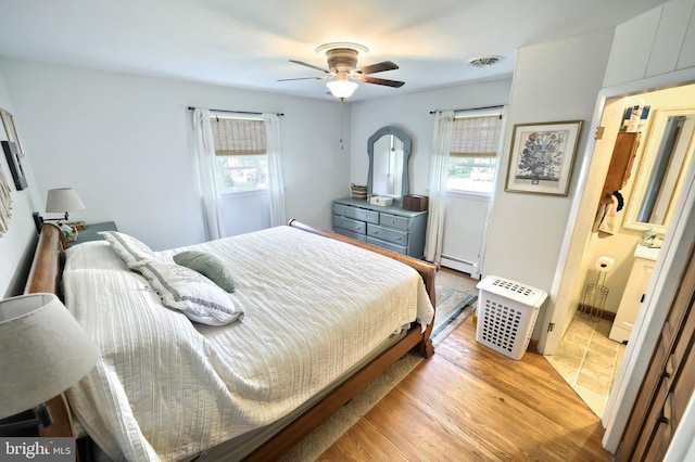 bedroom with light wood-type flooring, a ceiling fan, baseboard heating, and multiple windows