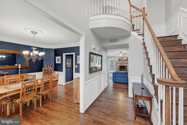 dining space featuring a decorative wall, stairs, wood finished floors, and ceiling fan with notable chandelier
