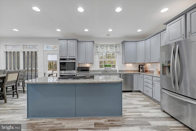 kitchen with gray cabinets, a center island, stainless steel appliances, and light stone counters