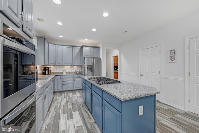 kitchen featuring light wood finished floors, stainless steel appliances, tasteful backsplash, a kitchen island, and blue cabinets