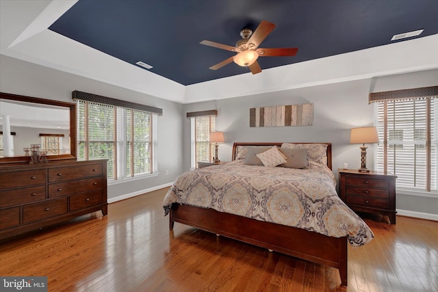 bedroom with baseboards, hardwood / wood-style flooring, a ceiling fan, and a raised ceiling