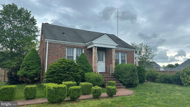 view of front facade with brick siding, fence, a front yard, and roof with shingles