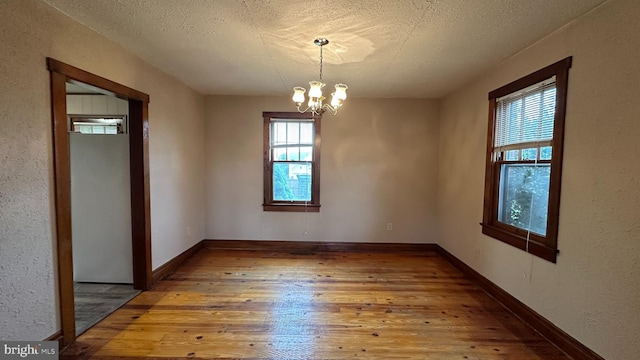 empty room with a chandelier, baseboards, a textured ceiling, and wood-type flooring
