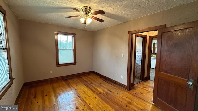 unfurnished room with a textured ceiling, light wood-style floors, a ceiling fan, and baseboards