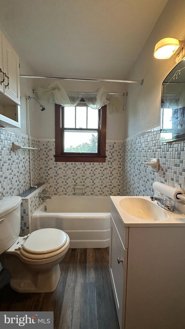 full bath with toilet, tile walls, shower / bathing tub combination, wood finished floors, and vanity