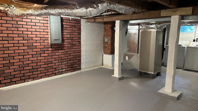 unfinished basement with electric panel, washing machine and clothes dryer, and brick wall
