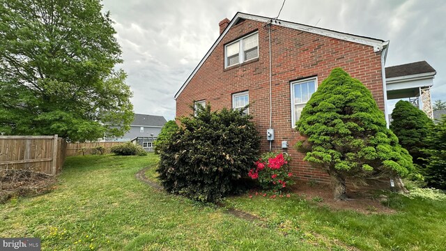 view of side of property featuring a chimney, brick siding, fence, and a lawn