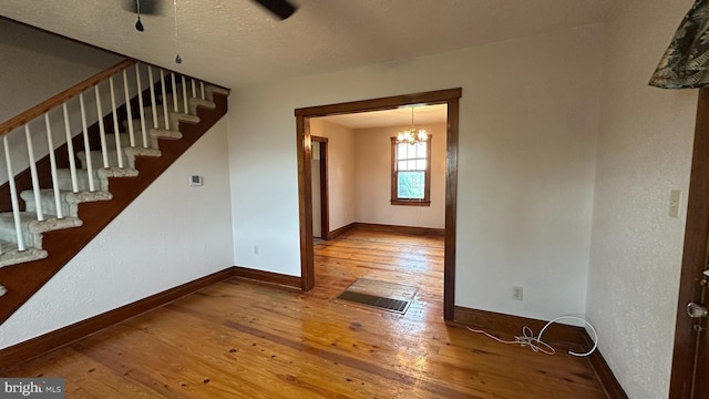 interior space with a chandelier, wood-type flooring, stairs, baseboards, and a textured ceiling
