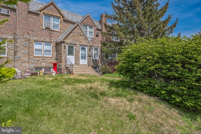 view of front facade with a chimney, entry steps, stone siding, a high end roof, and a front lawn