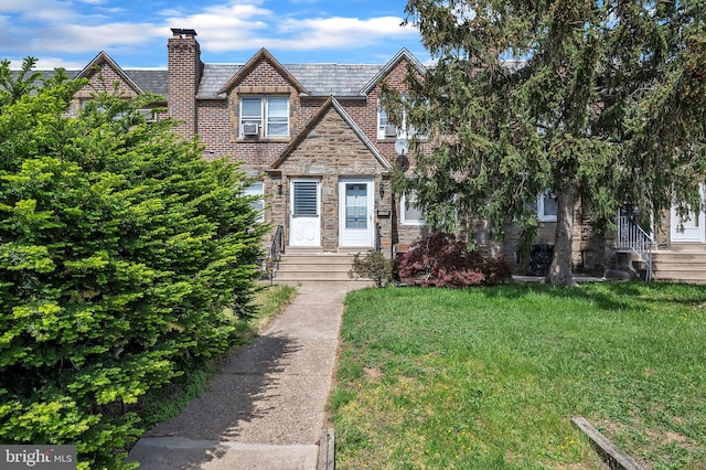 view of front of house with a chimney, brick siding, a front lawn, and stone siding