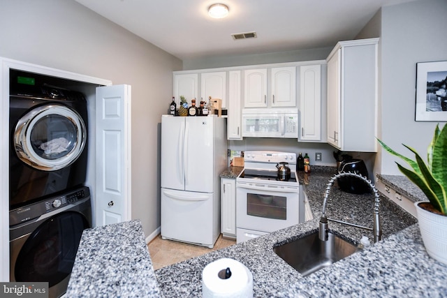 kitchen with visible vents, white appliances, stacked washing maching and dryer, dark stone counters, and white cabinets