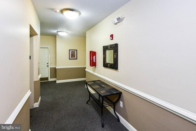 hall featuring baseboards and dark carpet