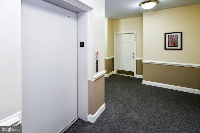 hallway with baseboards, elevator, and dark carpet