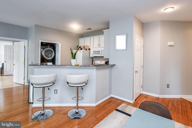 kitchen with visible vents, stacked washer / dryer, white appliances, baseboards, and light wood-style flooring