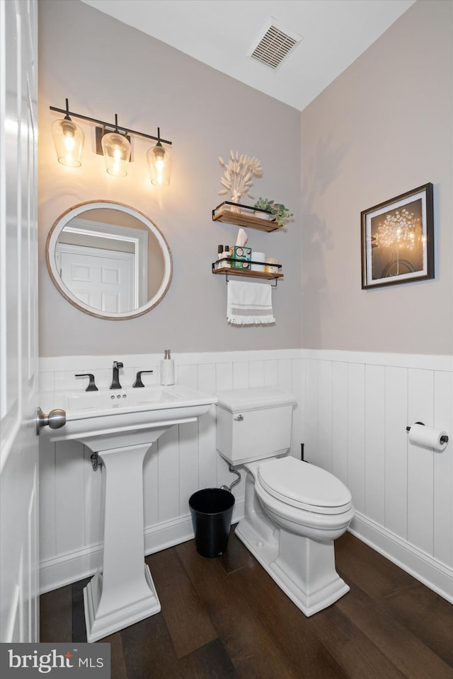 bathroom featuring toilet, visible vents, wood finished floors, and a wainscoted wall