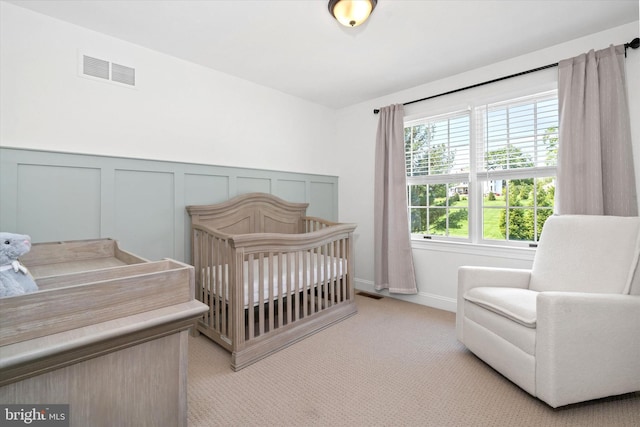 bedroom with wainscoting, light carpet, a crib, a decorative wall, and visible vents