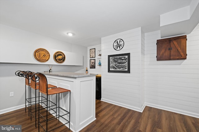 interior space with a peninsula, baseboards, a breakfast bar area, and dark wood finished floors