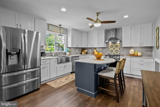 kitchen with wall chimney range hood, ceiling fan, dark wood-style flooring, a sink, and stainless steel appliances