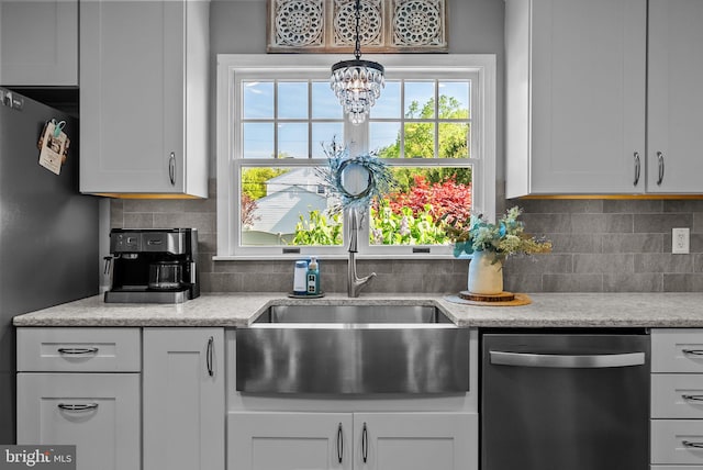 kitchen with tasteful backsplash, stainless steel dishwasher, a sink, white cabinets, and a chandelier