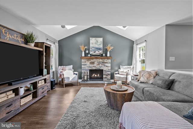 living area featuring dark wood-style flooring, vaulted ceiling with skylight, and a fireplace