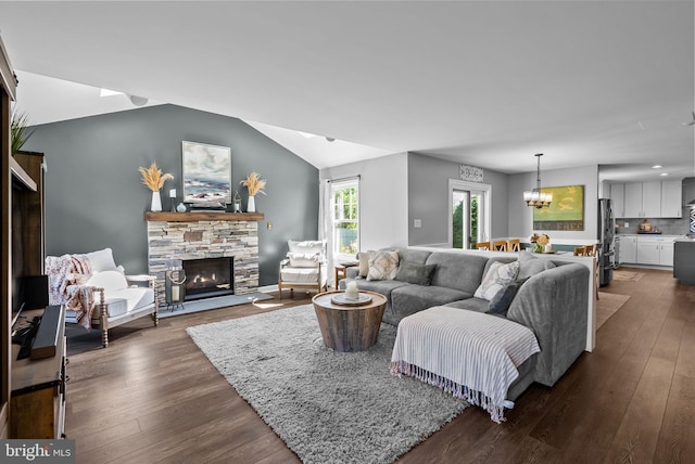 living room with vaulted ceiling, dark wood-style flooring, a stone fireplace, and a notable chandelier