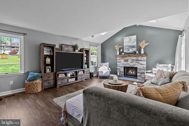 living area with baseboards, wood finished floors, vaulted ceiling with skylight, and a stone fireplace