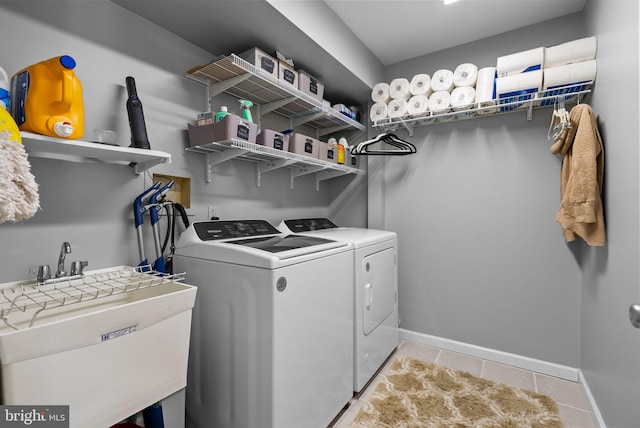 clothes washing area featuring laundry area, baseboards, washing machine and clothes dryer, a sink, and light tile patterned floors