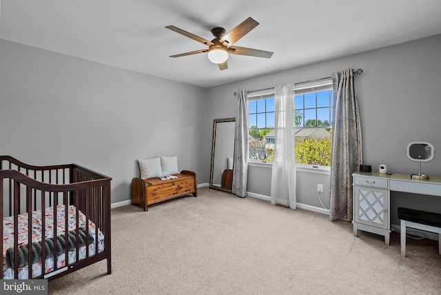bedroom featuring a nursery area, baseboards, carpet, and a ceiling fan