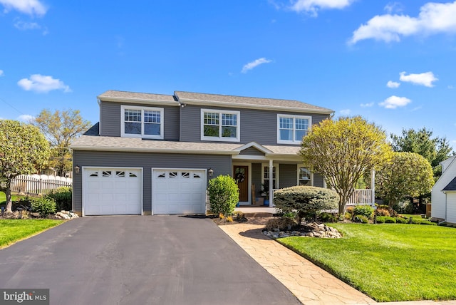traditional-style house with covered porch, aphalt driveway, a garage, fence, and a front lawn