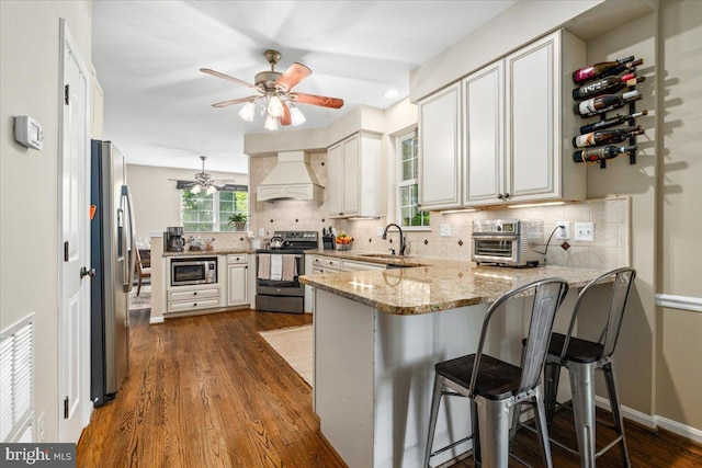 kitchen featuring a ceiling fan, backsplash, appliances with stainless steel finishes, a peninsula, and custom range hood