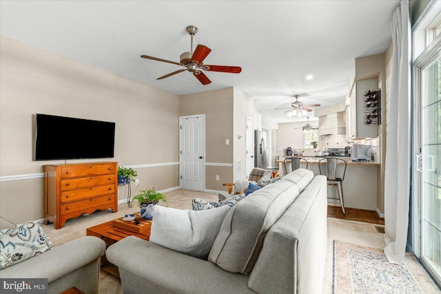 living room with ceiling fan, light carpet, and baseboards