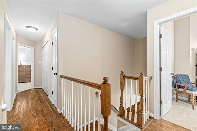hallway with baseboards, wood finished floors, and an upstairs landing