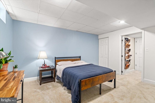 bedroom featuring baseboards, a drop ceiling, carpet, and a closet