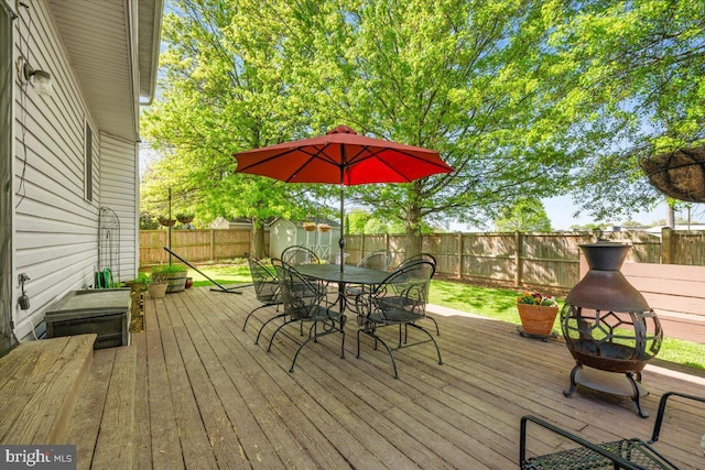 wooden terrace with an outbuilding, outdoor dining area, a fenced backyard, and a storage unit