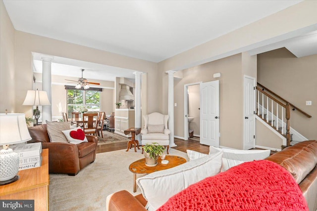 living area with ceiling fan, wood finished floors, stairway, baseboards, and ornate columns