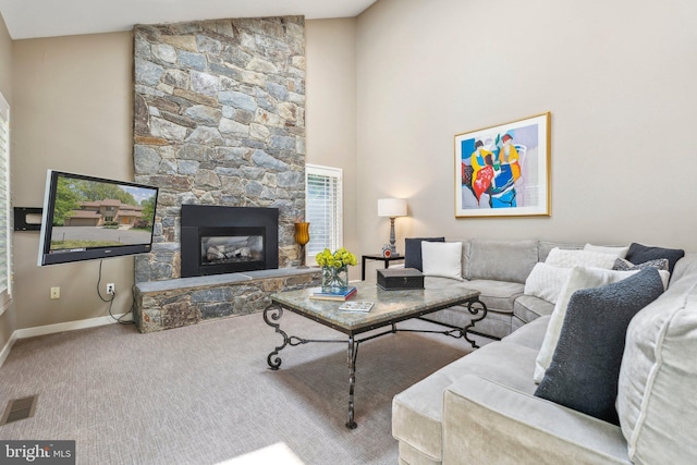 carpeted living room featuring baseboards, a high ceiling, a stone fireplace, and visible vents