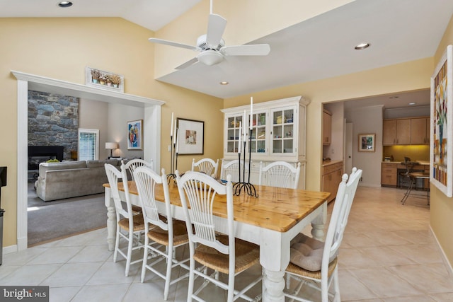 dining area featuring a stone fireplace, a ceiling fan, light tile patterned floors, and vaulted ceiling