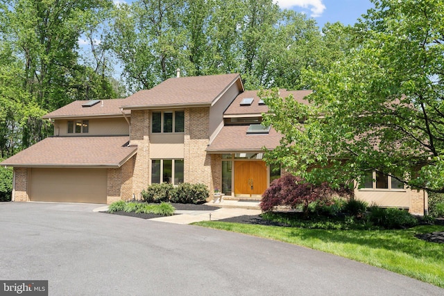 prairie-style house with a garage, aphalt driveway, roof with shingles, and brick siding