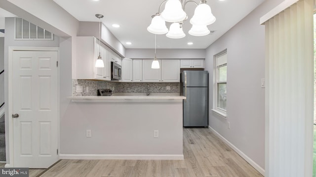 kitchen featuring appliances with stainless steel finishes, white cabinetry, light wood-style flooring, and backsplash